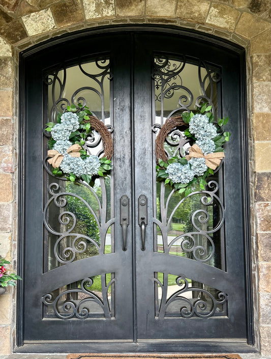 Mirror image pair of hydrangea wreaths on a set of elegant double doors with 6 large dusty blue hydrangeas on each wreath.