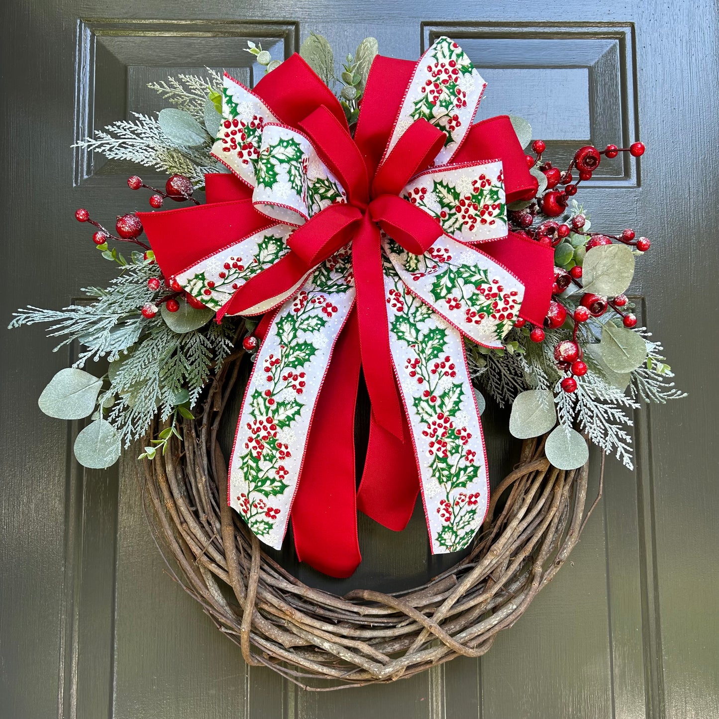 Wreath with round grapevine base, with red and holly ribbon and greenery.