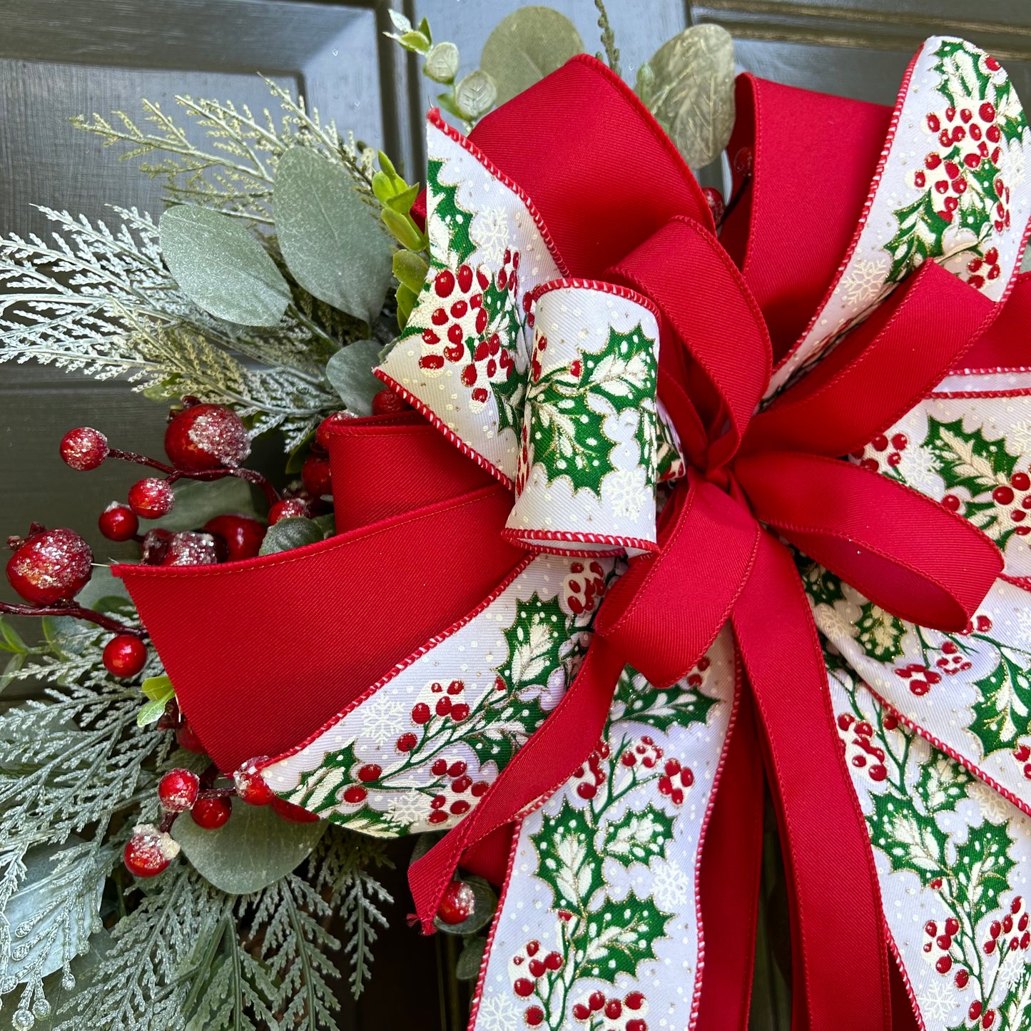 wreath with red ribbon and holly ribbon and greenery.