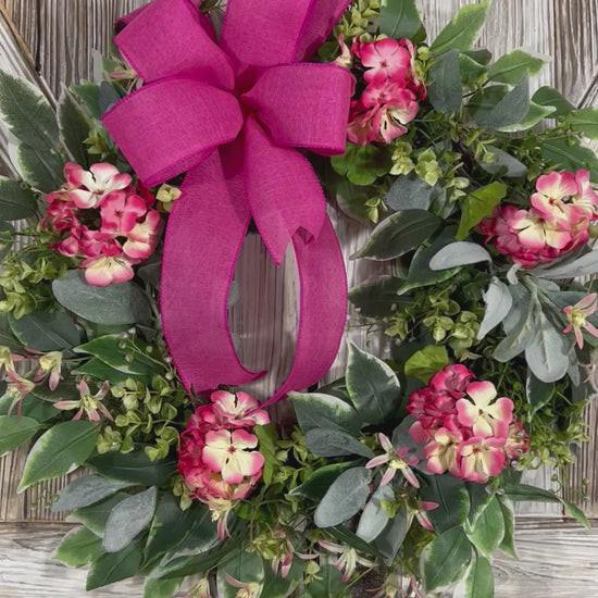 Video of summer geranium wreath featuring delicate geraniums in a soft pink hue accented with pale yellow details. Features a combination of ficus, boxwood, and lamb's ear greenery.