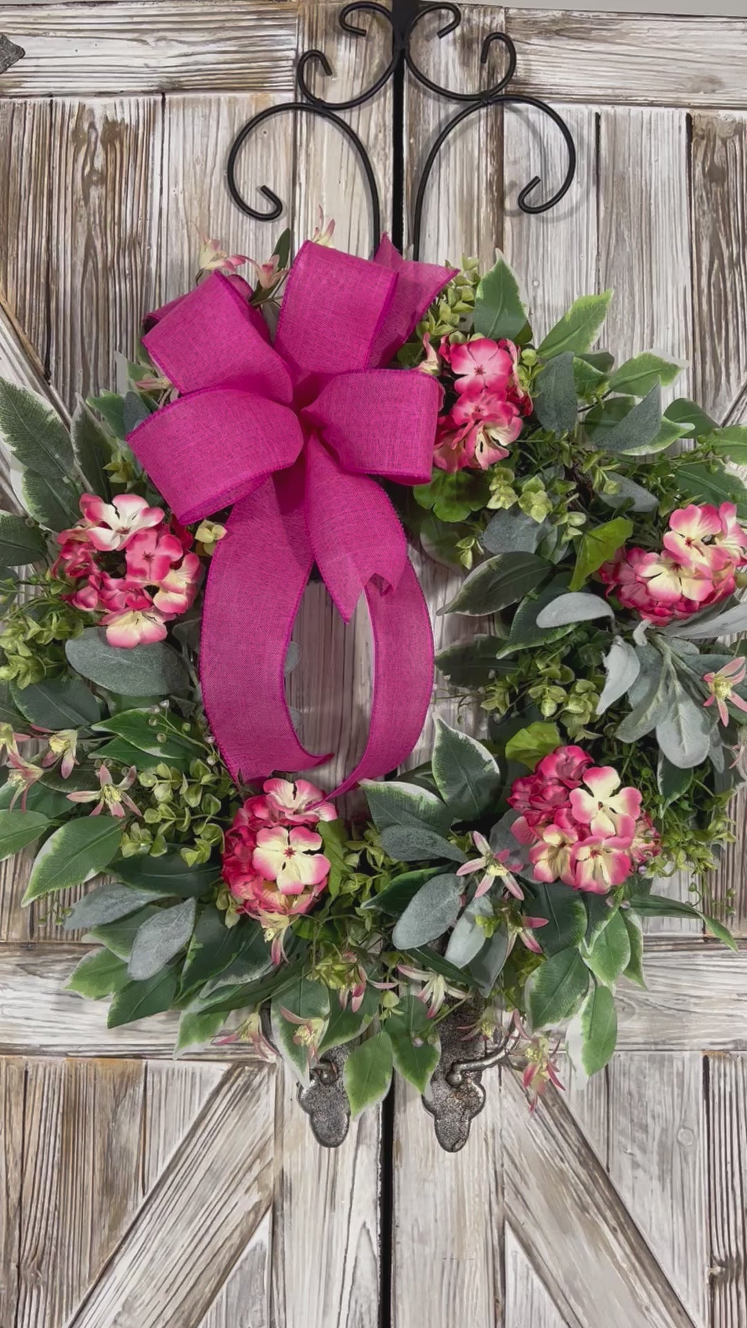 Video of summer geranium wreath featuring delicate geraniums in a soft pink hue accented with pale yellow details. Features a combination of ficus, boxwood, and lamb's ear greenery.