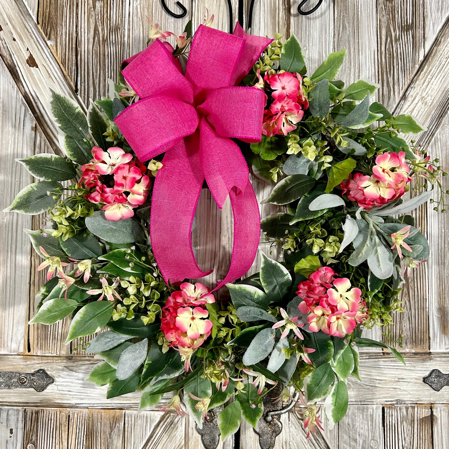 Summer geranium wreath featuring delicate geraniums in a soft pink hue accented with pale yellow details. Features a combination of ficus, boxwood, and lamb's ear greenery.